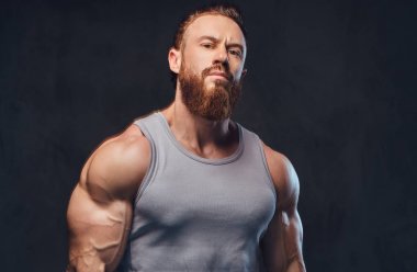 Gri arka plan üzerinde izole bir kolsuz gömlek giymiş acımasız sakallı vücut geliştirmeci portresi.