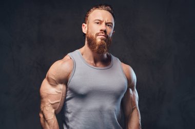 Gri arka plan üzerinde izole bir kolsuz gömlek giymiş acımasız sakallı vücut geliştirmeci portresi.