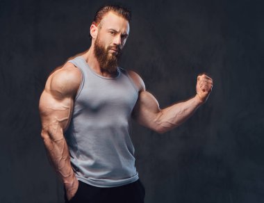 Gri arka plan üzerinde izole bir kolsuz gömlek giymiş acımasız sakallı vücut geliştirmeci portresi.