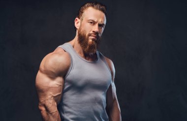 Gri arka plan üzerinde izole bir kolsuz gömlek giymiş acımasız sakallı vücut geliştirmeci portresi.