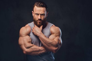 Gri arka plan üzerinde izole bir kolsuz gömlek giymiş acımasız sakallı vücut geliştirmeci portresi.