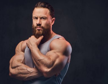Gri arka plan üzerinde izole bir kolsuz gömlek giymiş acımasız sakallı vücut geliştirmeci portresi.