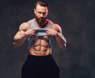 Gri arka plan üzerinde izole bir kolsuz gömlek giymiş acımasız sakallı vücut geliştirmeci portresi.