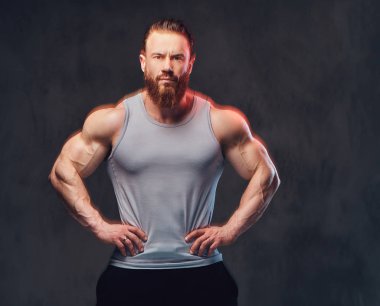 Gri arka plan üzerinde izole bir kolsuz gömlek giymiş acımasız sakallı vücut geliştirmeci portresi.