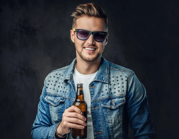 积极的金发男子穿着牛仔夹克和太阳镜持有一瓶工艺啤酒 — 图库照片