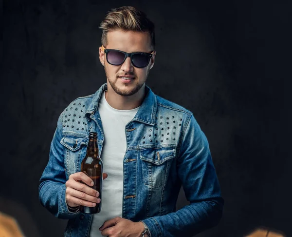 デニム ジャケットとサングラスに身を包んだ肯定的な金髪男性がクラフト ビールの瓶を保持しています — ストック写真