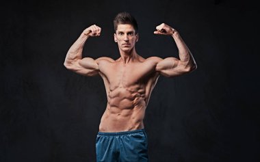 Stüdyo portre ectomorph kas gömleksiz erkek onun pazı koyu gri arka plan üzerinde gösterir..