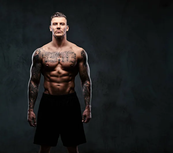 A muscular tattooed man on a dark background. — Stock Photo, Image