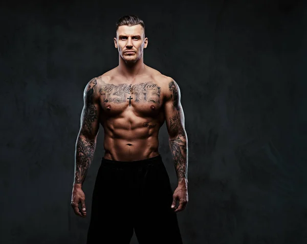 Un homme tatoué musclé sur un fond sombre . — Photo