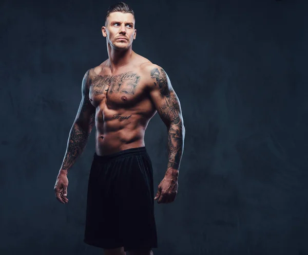 Um homem tatuado muscular em um fundo escuro . — Fotografia de Stock