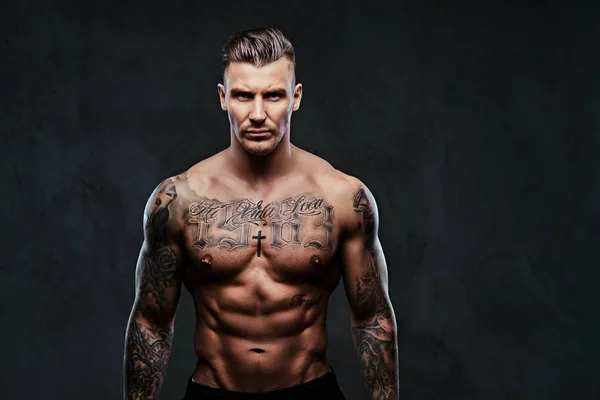 Un homme tatoué musclé sur un fond sombre . — Photo