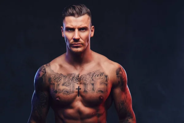 Un uomo muscoloso tatuato su uno sfondo scuro . — Foto Stock