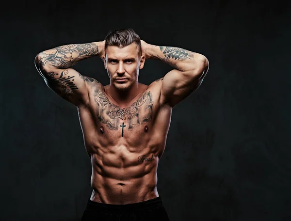 Un hombre musculoso tatuado sobre un fondo oscuro . —  Fotos de Stock