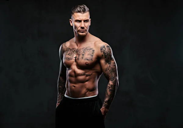 Um homem tatuado muscular em um fundo escuro . — Fotografia de Stock