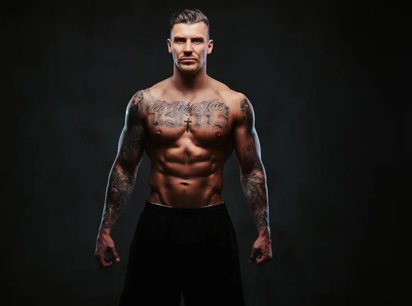 En muskulös tatuerad man på en mörk bakgrund. — Stockfoto