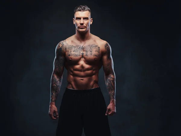 Мускулистый татуированный человек на тёмном фоне . — стоковое фото