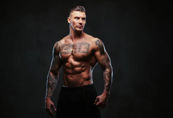 Мускулистый татуированный человек на тёмном фоне . — стоковое фото