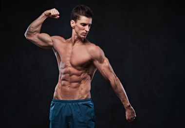 Stüdyo portre ectomorph kas gömleksiz erkek onun pazı koyu gri arka plan üzerinde gösterir..