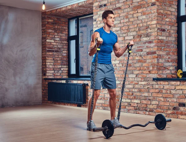 Muscular male doing biceps exercises with barbell in a club with loft interior.