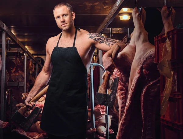 Portrait of a butcher in an apron holds an ax in a meat factory.