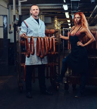 Portrait of a chef and his female helper in a sausage storage. clipart