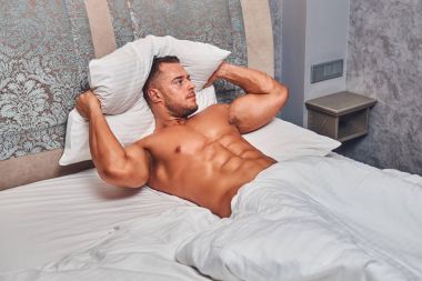 Gömleksiz seksi kaslı erkek model uzağa bakarak onun yatak odasında onun yatakta yalnız yatarken.