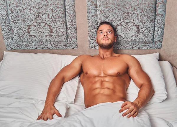 赤裸上身性感的肌肉男模特独自躺在床上 在他的卧室 看着远 — 图库照片