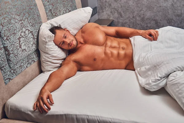 Un bel uomo nudo sdraiato in un letto . — Foto Stock