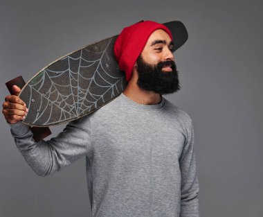 Kırmızı bir şapka ve güneş gözlüğü ile omuz kaykay sakallı hippi erkek portresi.