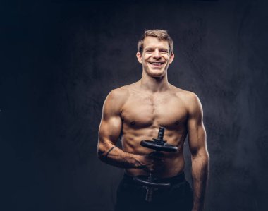 Koyu arka plan üzerinde pazı egzersizleri yapıyor bir spor şort giymiş bir gülümseyen gömleksiz atletik dövmeli erkek portresi stüdyo.