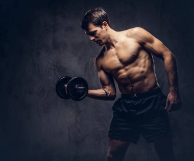 Stüdyo portre gömleksiz atletik dövmeli erkek üzerinde koyu arka plan üzerinde pazı egzersizleri yapıyor bir spor şort giymiş.