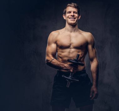 Koyu arka plan üzerinde pazı egzersizleri yapıyor bir spor şort giymiş bir gülümseyen gömleksiz atletik dövmeli erkek portresi stüdyo.