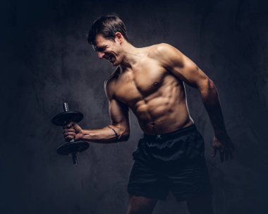 Koyu arka plan üzerinde pazı egzersizleri yapıyor bir spor şort giymiş bir gülümseyen gömleksiz atletik dövmeli erkek portresi stüdyo.