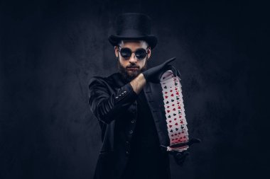 İskambil ile hüner karanlık bir arka plan üzerinde gösterilen sihirbaz siyah bir takım elbise, güneş gözlüğü ve şapka,.