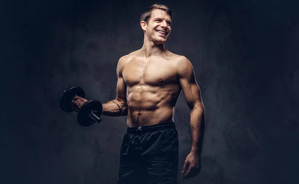 暗い背景上の上腕二頭筋のエクササイズ スポーツ ショート パンツに身を包んだ笑顔上半身裸運動刺青男性のスタジオ ポートレート — ストック写真