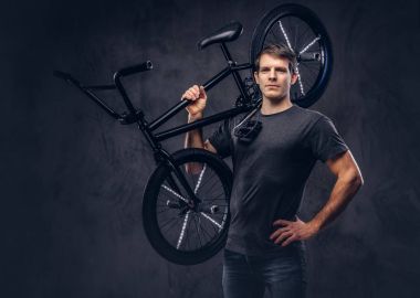T-shirt ve kot Bmx bisiklet üzerinde omzunun karanlık bir arka plan üzerinde tutarak gülümseyen yakışıklı.