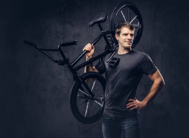 T-shirt ve kot Bmx bisiklet üzerinde omzunun karanlık bir arka plan üzerinde tutarak gülümseyen yakışıklı.
