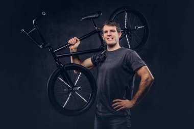 T-shirt ve kot Bmx bisiklet üzerinde omzunun karanlık bir arka plan üzerinde tutarak gülümseyen yakışıklı.