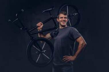 T-shirt ve kot Bmx bisiklet üzerinde omzunun karanlık bir arka plan üzerinde tutarak gülümseyen yakışıklı.
