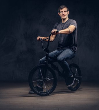 T-shirt ve kot bir Bmx. göl kenarında koyu arka plan üzerinde oturan yakışıklı adam.