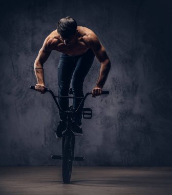 Güçlü gömleksiz adam, bir stüdyoda Bmx ile akrobatik bir şekil yapar. Karanlık bir arka plan üzerinde izole.