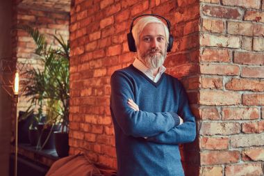 Yakın çekim yakışıklı bir komuta sizde çatı iç ile bir odada bir tuğla duvara yaslanmış kulaklık müzik dinlemek portresi.