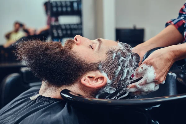 Professional hairdresser washing client hair in a barbershop.