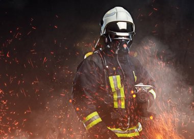 Profesyonel bir itfaiyeci üniforması giymiş ve yangın bir oksijen maskesi ayakta kıvılcım ve karanlık bir arka plan üzerinde duman.