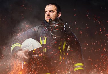 Profesyonel bir itfaiyeci karanlık bir arka plan üzerinde düzgün güvenlik kask yangında kıvılcım holding ve duman giymiş.