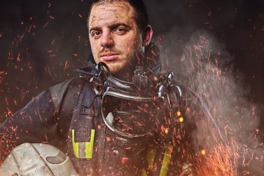 Profesyonel bir itfaiyeci karanlık bir arka plan üzerinde düzgün güvenlik kask yangında kıvılcım holding ve duman giymiş.