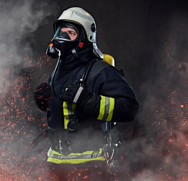 身着制服的消防员肖像和一个氧气面罩站在火的火花和烟雾在黑暗的背景下 — 图库照片