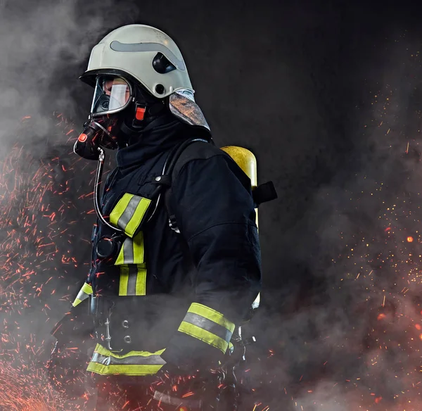 一名职业消防员身着制服和氧气面罩站在火灾火花和烟雾在黑暗的背景下 — 图库照片