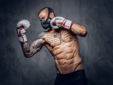 Stüdyo portre gömleksiz, dövme maskeli savaşçı erkek gri vignette arka plan üzerinde.