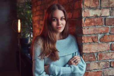 Çatı katı iç ile bir odada bir tuğla duvara yaslanmış bir gri süveterli şehvetli bir esmer.